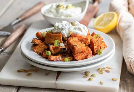 A plate of roasted sweet potatoes topped with yogurt and scallions