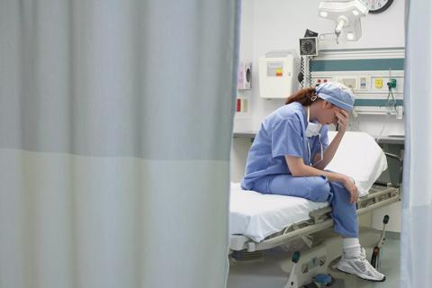 View through privacy curtains to female doctor sitting with head in hand