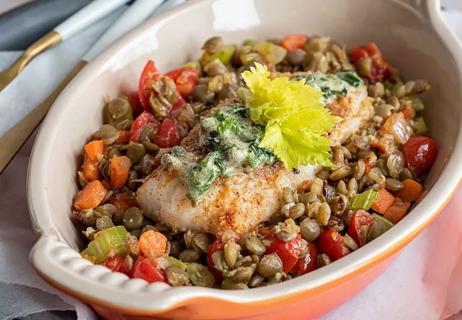 A casserole dish filled with lentils, vegetables and cod