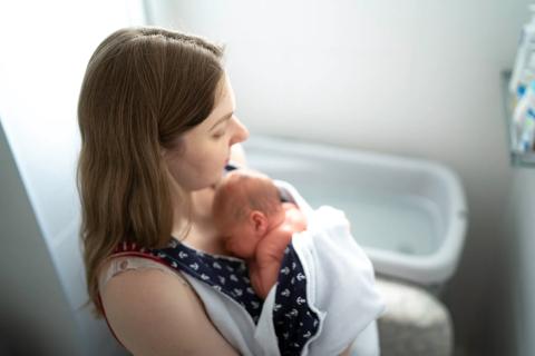 Caregiver holding newborn on chest, with bathtub filling in background