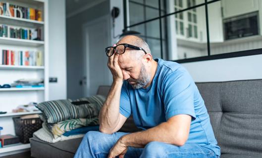 Man sitting on couch, glasses pushed up on forehead, rubbing their closed eyes