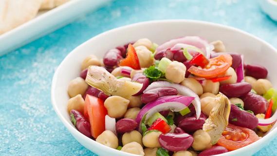 Salad with vegetables, chickpeas and artichokes in white bowl on a light blue table