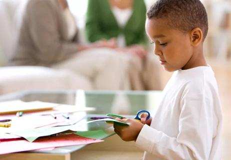 Little boy cutting paper with scissors at home