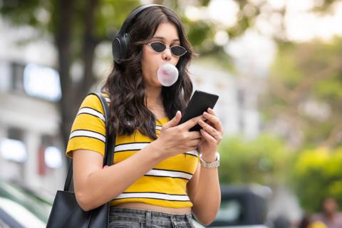 Person blowing a bubble with gum, walking, looking at cell phone