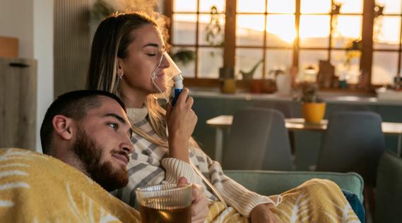 Person using a nebulizer, sitting on couch with loved one