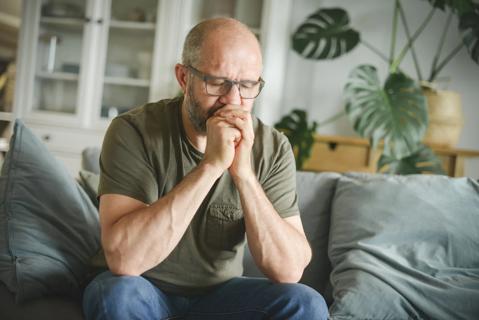 Older person sitting on couch with hands clenched, eyes closed