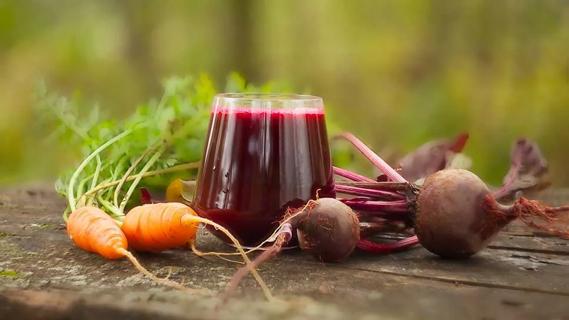 beet and carrot juice in a glass surrounded by beets and carrots