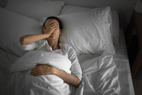 Person lying in bed in early morning, with hand on their head