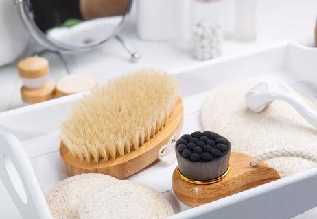 Skin care tools like a dry brush and exfoliating pads sit in a white tray atop a bathroom vanity