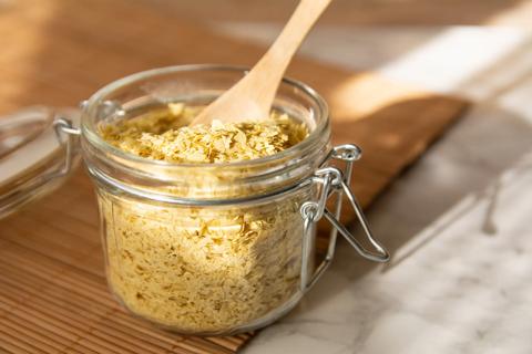 Glass jar of nutritional yeast with wooden spoon in it