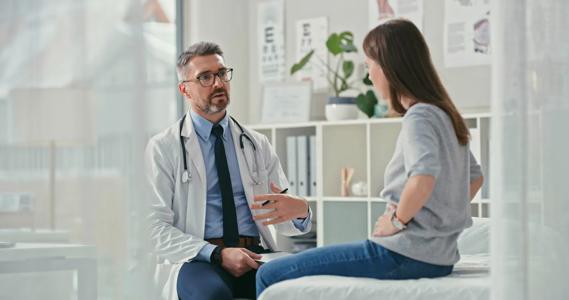 A doctor engages with a patient, who’s sitting on a medical exam table