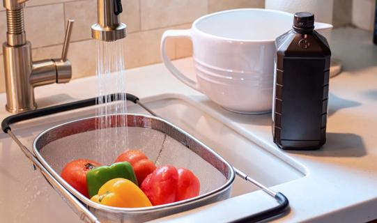 Veggies in strainer in sink with water running, with bottle of hydrogen peroxide and mixing bowl on counter