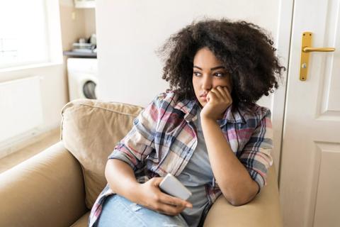 Female sitting in chair at home staring into the distance, phone in hand