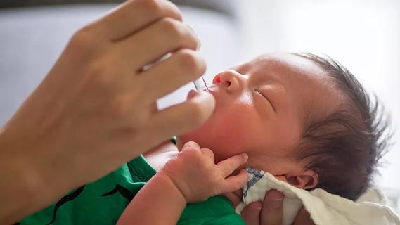Adult hand uses a dropper to deliver a liquid to newborn by mouth