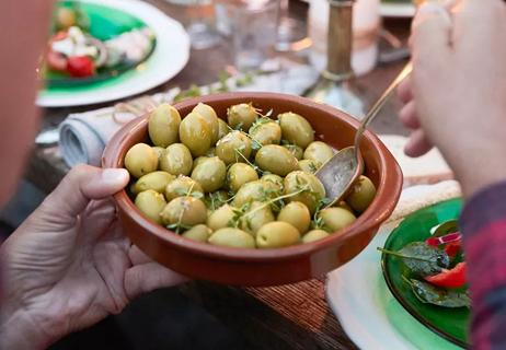 Person taking a helping of green olives at the dinner table.
