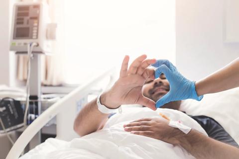 Patient in hospital bed and healthcare provider joining fingers to make a heart