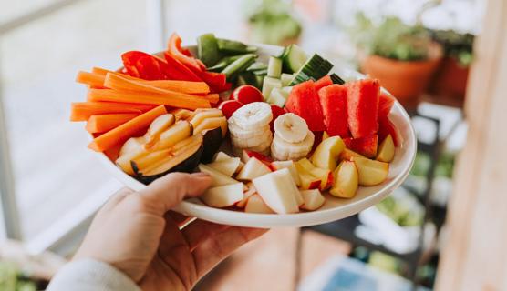 Hand holding platter of cut up fruits and veggies