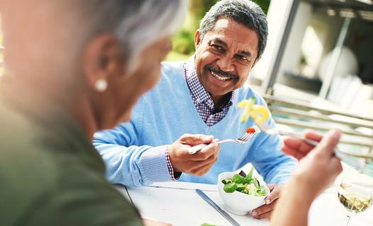 A smiling older man eating a salad at a table outside