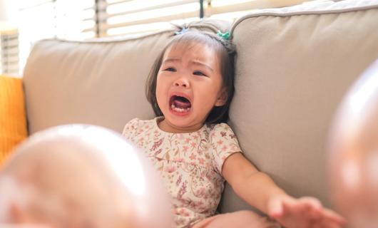 Toddler sitting on couch, crying, having a tantrum