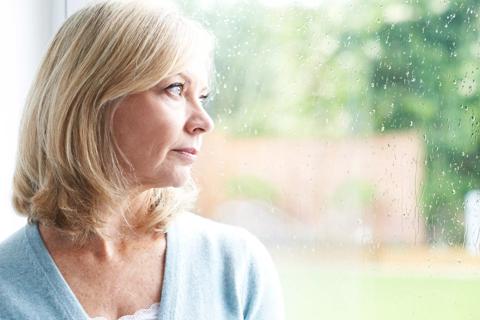 An forlorn individual looks out a window on a rainy day