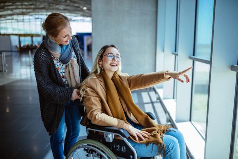 Smiling caretaker pushing smiling person in wheelchair at the airport, looking out the window