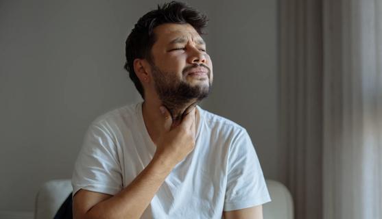 person sitting down, holding their hand to their throat