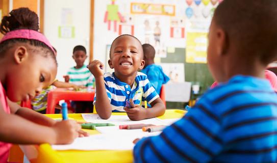 Kindergarten-age children coloring at table, with one child smiling