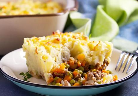A piece of shepherd's pie on a plate that has mashed potatoes, vegetables and meat