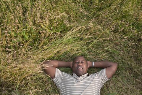 Person smiling, lying back, eyes closed, relaxing in long grass
