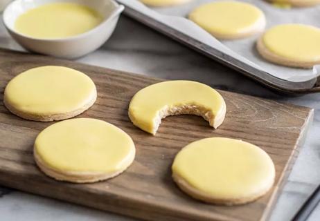 Round sugar cookies, one with a bite taken out of it, frosted with a thin glaze of yellow icing