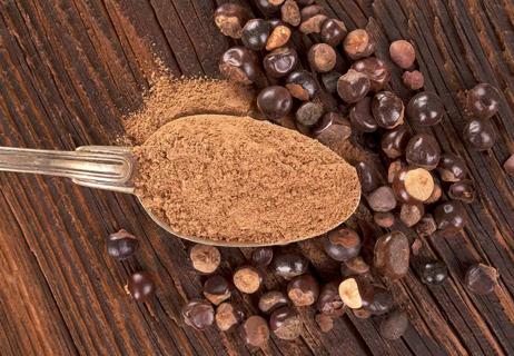 Guarana seeds in the background on a wooden table with a spoonful of powdered gurarana suspended above.