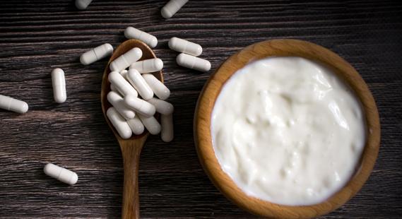 Wooden bowl of white yogurt next to wooden spoon of white capsules