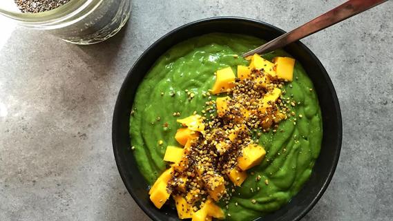 Top view of green smoothie bowl topped with mango and seeds on a granite counter