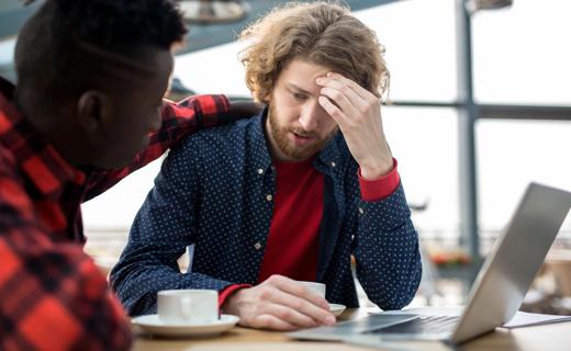 Person comforting stressed out person, with coffee cups and open laptop on table