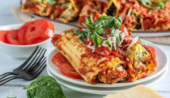 Two tofu-stuffed manicotti displayed on a bed of sliced tomatoes