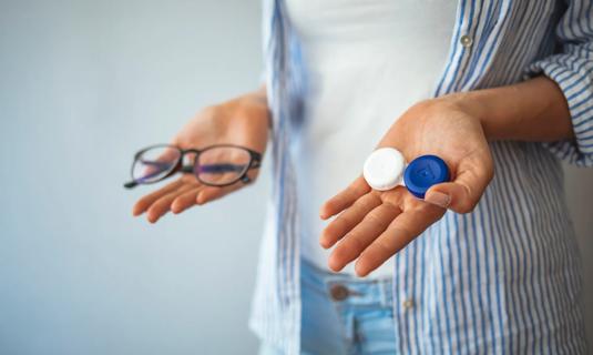 Person holding contact lenses case in one hand and glasses in the other hand