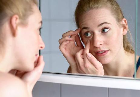 Woman examining puffy eye in mirror