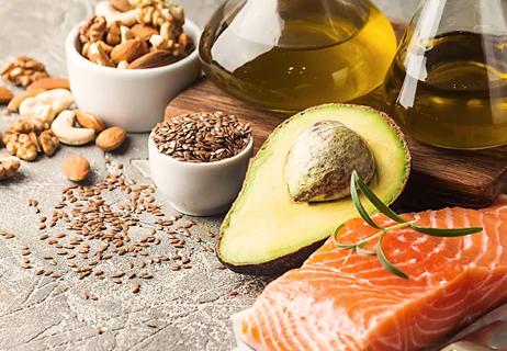 Raw salmon is displayed next to an avocado, various nuts and bottles of olive oil.