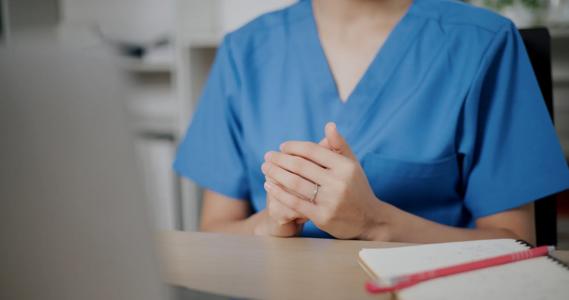 Person in scrubs with hands folded, across from person at desk