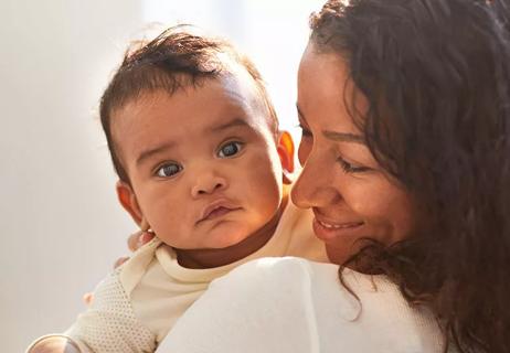 Baby facing camera held by happy mother