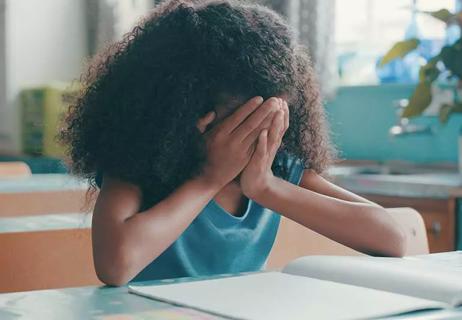 Child holding head in hands at school desk