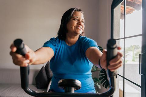 Smiling person on exercise equipment, looking out window while working out