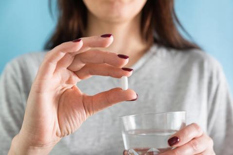 Person holding up a pill in hand and water in other hand