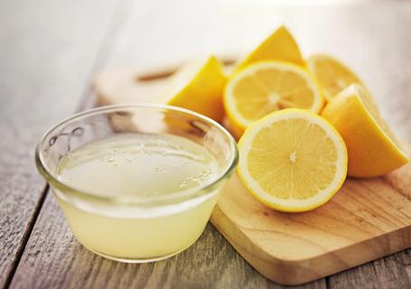 Halved lemons on cutting board next to glass bowl of lemon juice