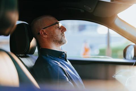 Person sitting in driver’s seat of car, with eyes closed and head back