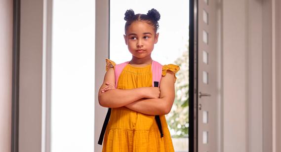 Child wearing backpack, standing with arms crossed