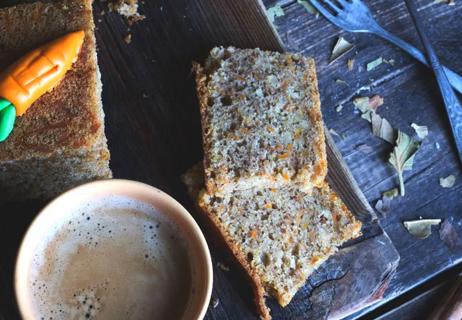 Healthier carrot cake on wooden platter with coffee in foreground.