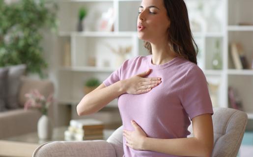 Person sitting with hand on abdomen and chest, taking slow, controlled breaths