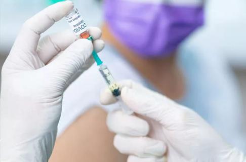 Medical professional in gloves prepares a syringe of a COVID vaccine for a person wearing a mask