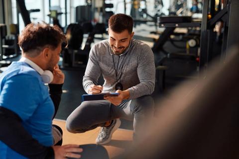 Fitness trainer with client, going over notes on clipboard in gym